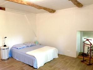 Un dormitorio con cama, lámpara de noche, cubo de basura y techo con vigas de madera.