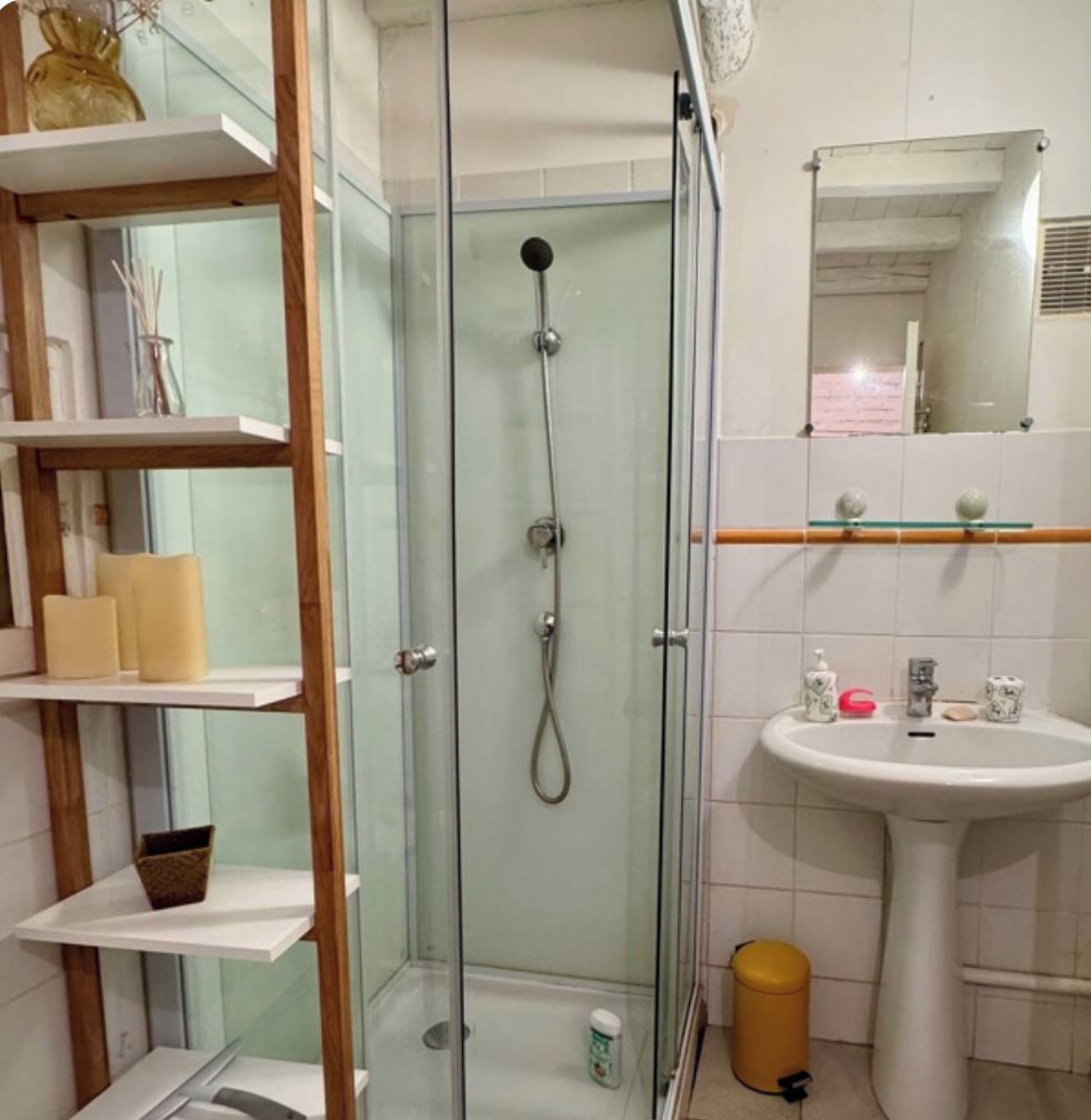 A bathroom with a glass-enclosed shower, a sink with toiletries, and a mirror.