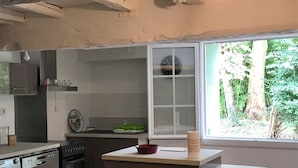 A kitchen with a washing machine, oven, and a window with a view of greenery. - Grand Mas, 32 hectares, nature and reunion (Mirepoix)