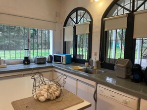 A kitchen with a window, a toaster, a kettle, a microwave, a sink, and a dish rack.