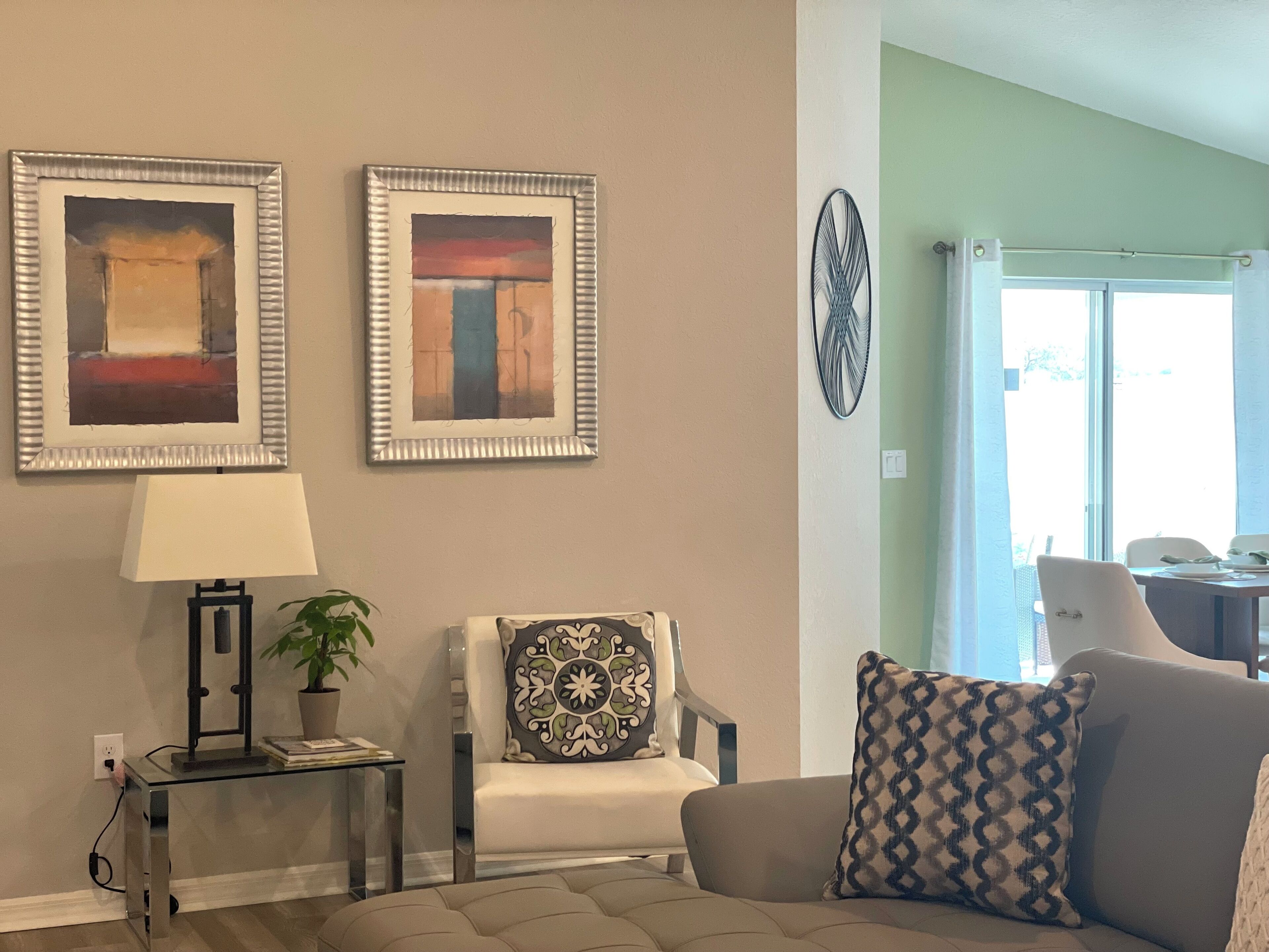 A living room with a sofa, a chair, a table with a lamp, and two framed artworks on the wall.
