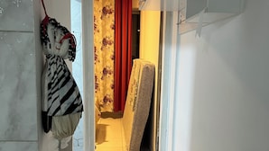 Een smalle gang met een betegelde vloer, een rood gordijn en een matras die tegen de muur staat.