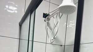 Een douche met een glazen deur, witte betegelde wanden en een witte douchekop.