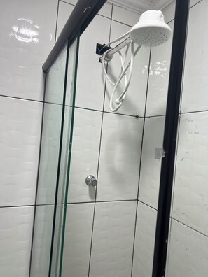 Eine Dusche mit Glastür, weißen Fliesen und einem weißen Duschkopf.