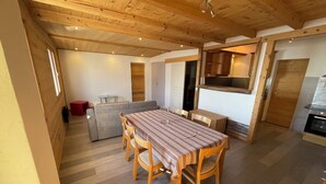 A dining area with a wooden table and chairs, a grey sofa, and a kitchen area with wooden cabinets and a stove. - Superb apartment in a country house (Passy)