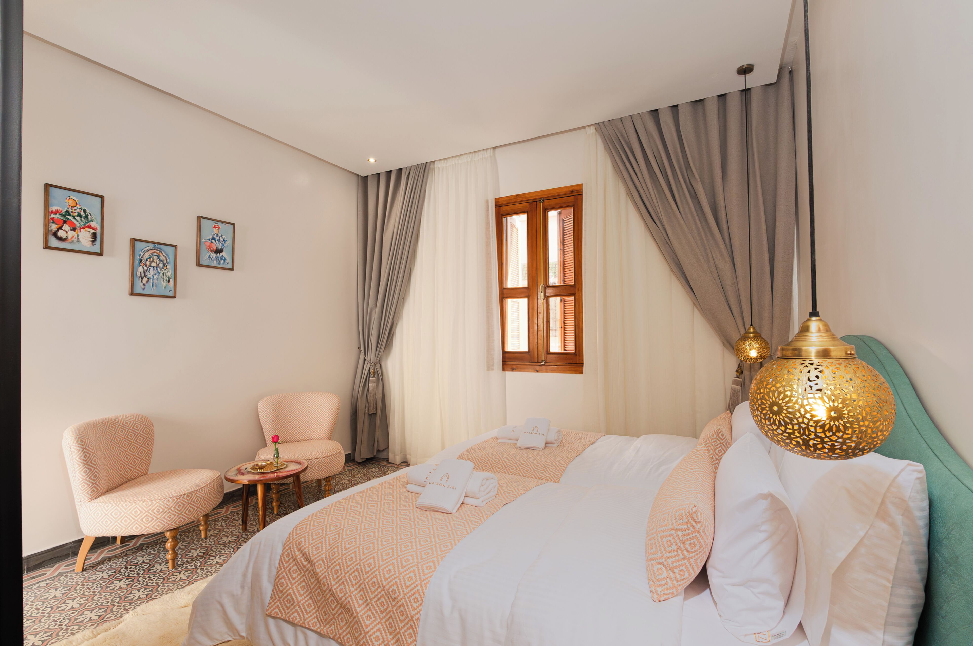 Una camera d'hotel con un letto, due poltrone, un tavolino, una finestra con tende e decorazioni alle pareti.
