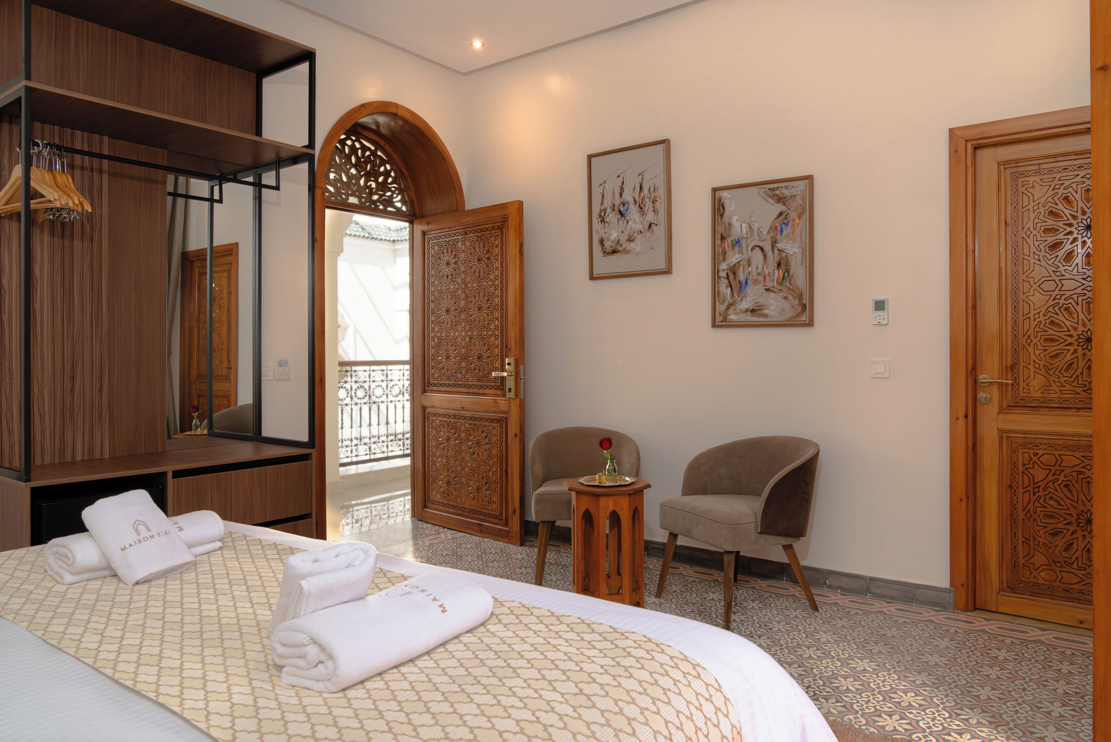 A hotel room with a bed, two chairs, a small table with a vase, and a wooden wardrobe.