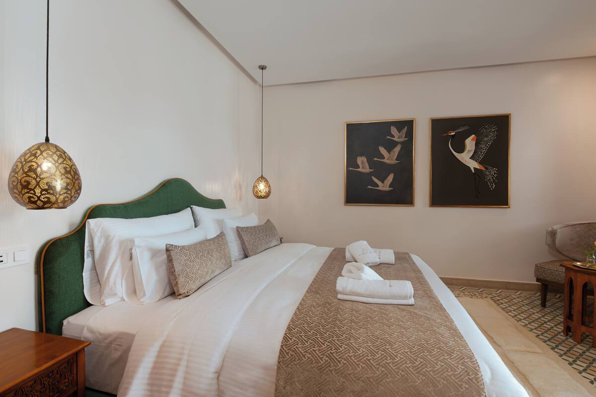 A neatly made bed with a patterned bedspread, a green headboard, and a pair of towels on the side.