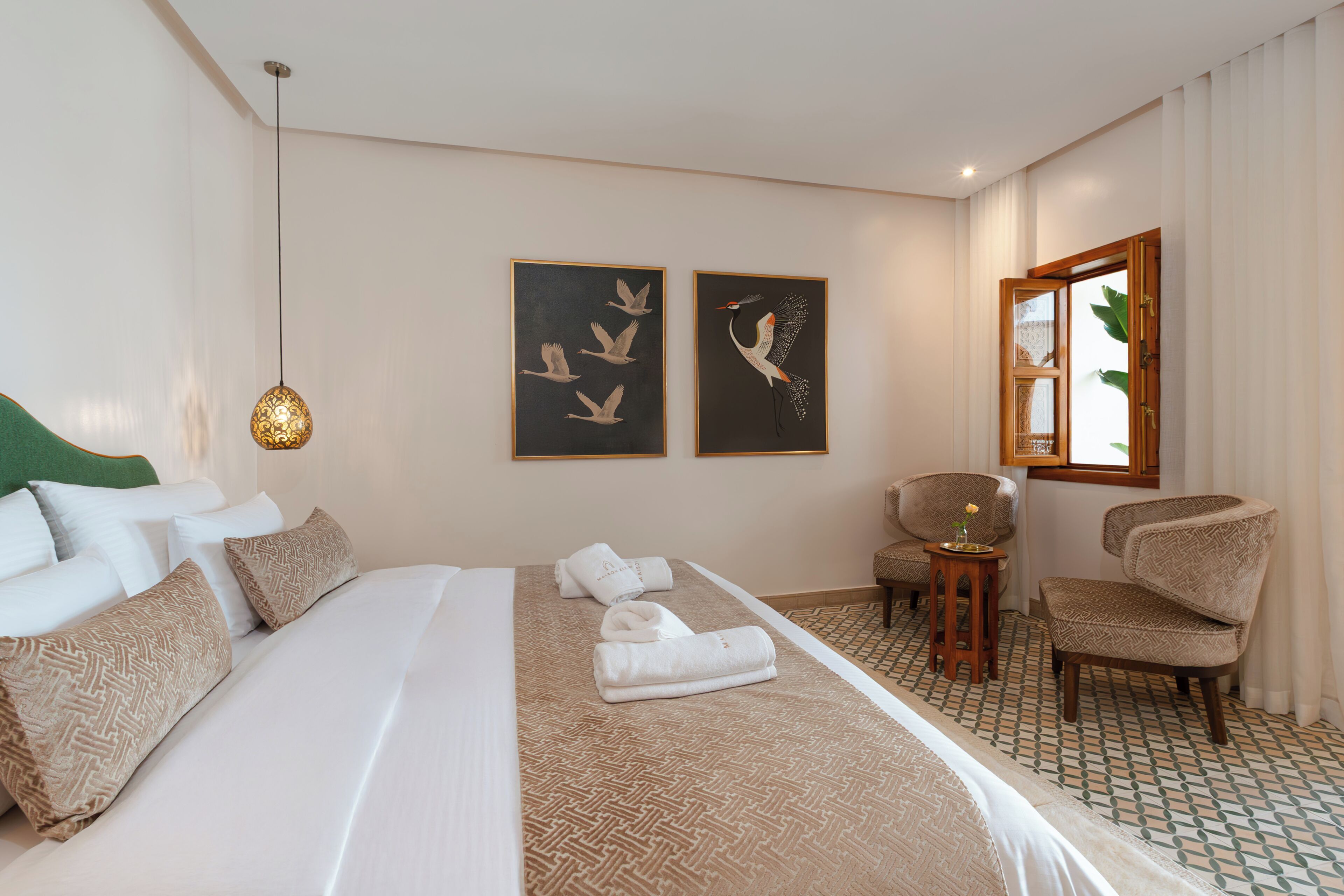 A hotel room with a large bed, two chairs, a small table, and artwork on the wall.