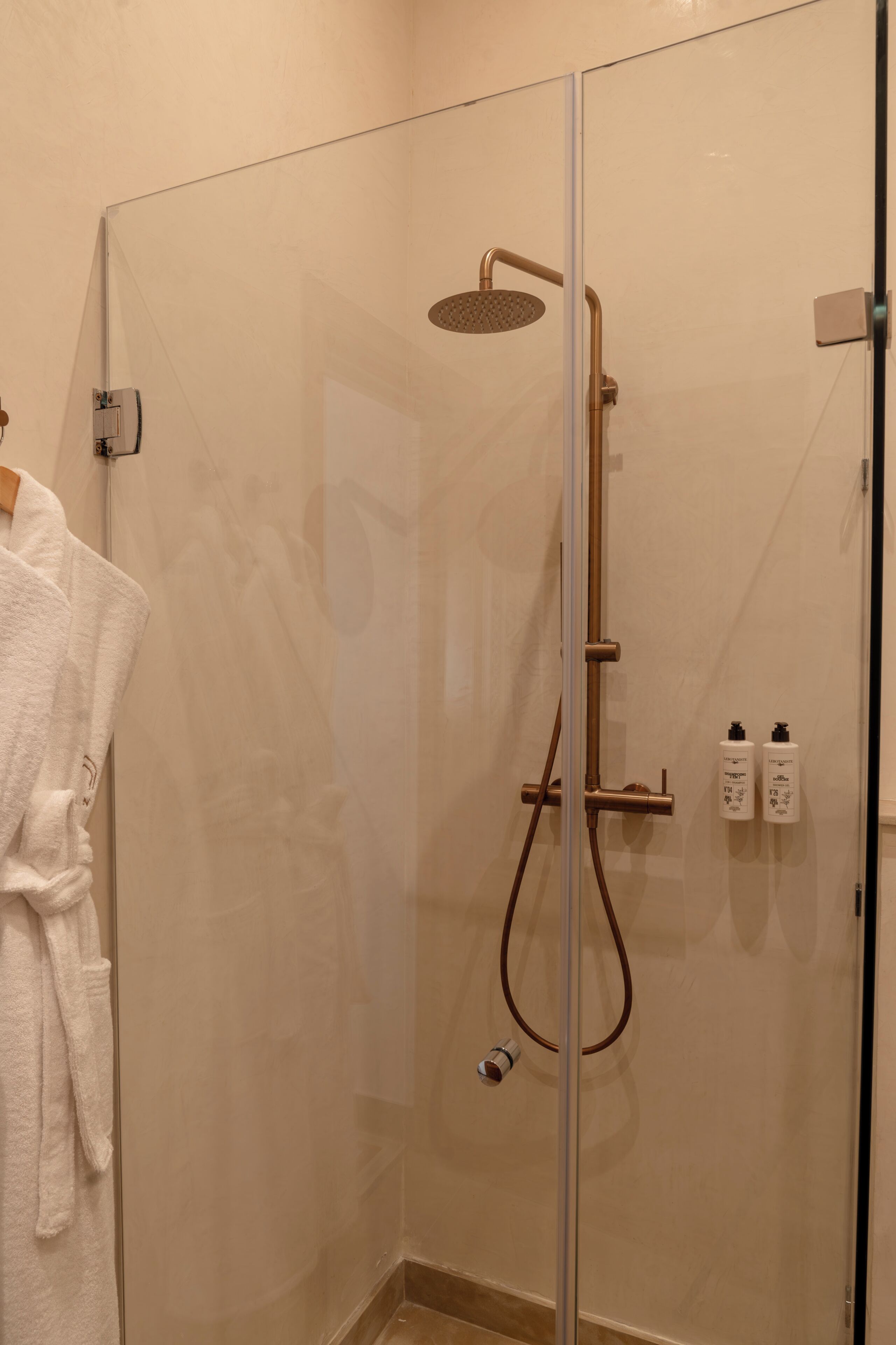 A glass-enclosed shower with a handheld showerhead and a wall-mounted control panel.