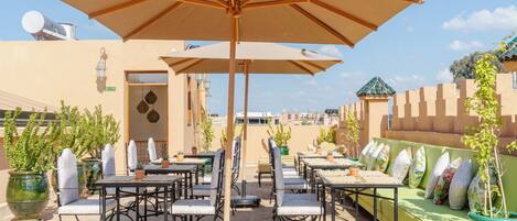 An outdoor seating area with tables and chairs, umbrellas, and potted plants.