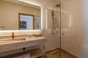 Un baño moderno con ducha envuelta en vidrio, un espejo grande y encimera de mármol.