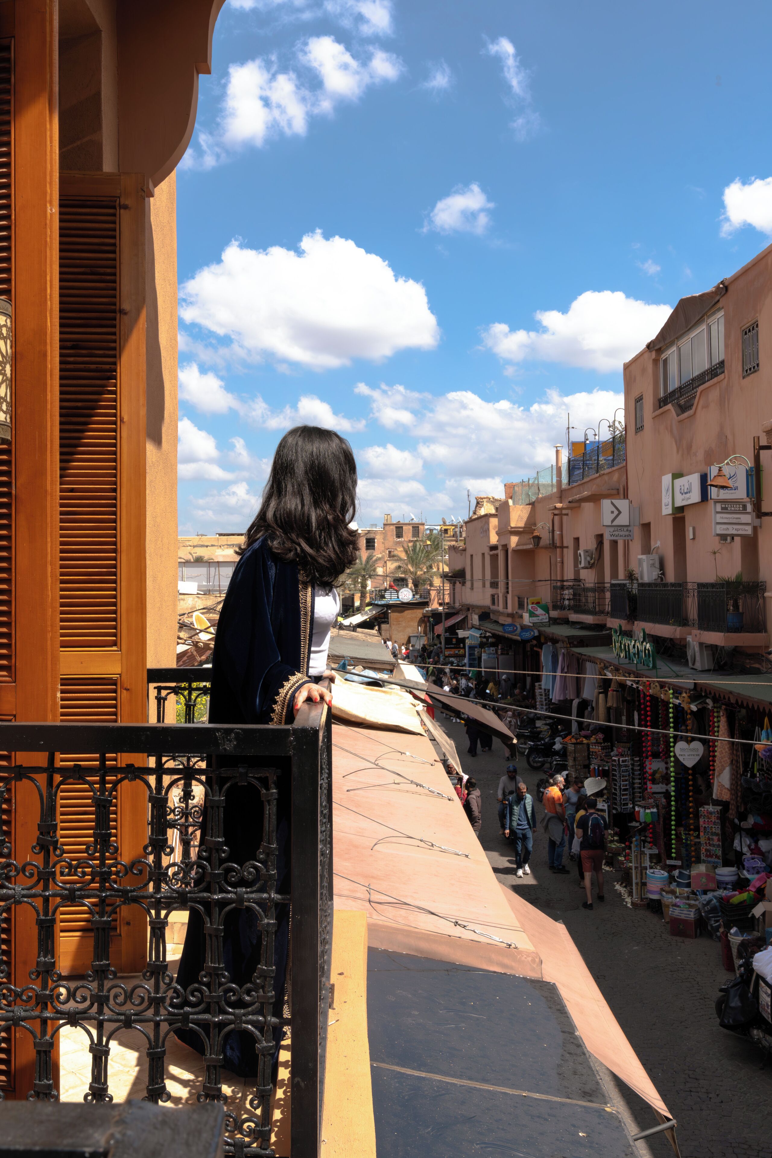 A balcony overlooking a bustling street with shops and pedestrians.