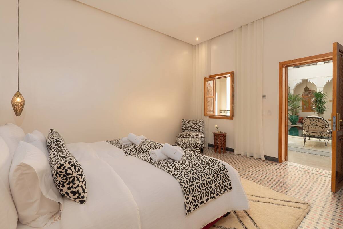 A hotel room with a bed, a chair, a small table, and a mirror.