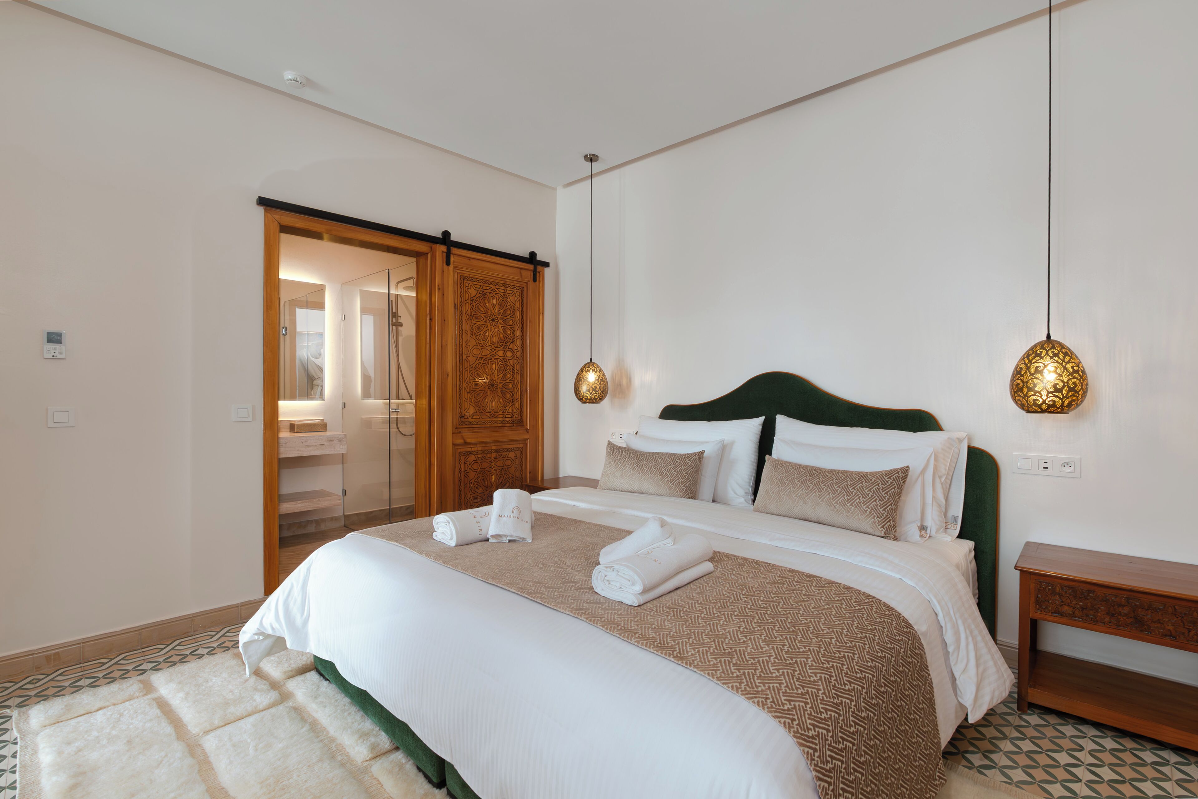 A neatly made bed with a patterned bedspread, a wooden headboard, and a bedside table with a lamp.