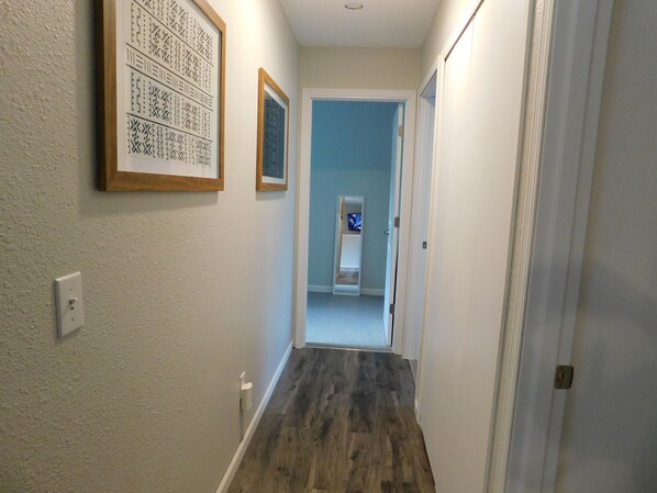 A narrow hallway with patterned wall decorations, a door leading to a room with a bed and a television, and a light switch on the wall.