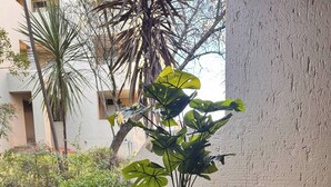 A patio with a table and two chairs, a potted plant, and a view of a building and greenery. - Stylish 1-bed in Bryanston (Johannesburg)