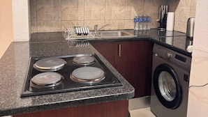 A compact kitchen with a stove, sink, and washing machine. - Stylish 1-bed in Bryanston (Johannesburg)