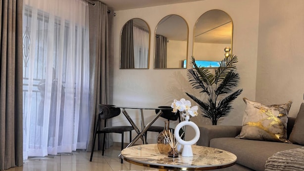 A modern living room with a round coffee table, a sofa, a chandelier, and a dining area with chairs and a table. - Stylish 1-bed in Bryanston (Johannesburg)