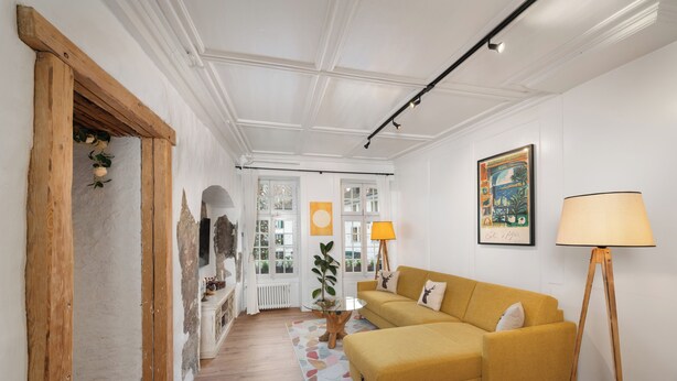 Ein Wohnzimmer mit gelbem Sofa, einer Stehlampe und einem gemusterten Teppich.