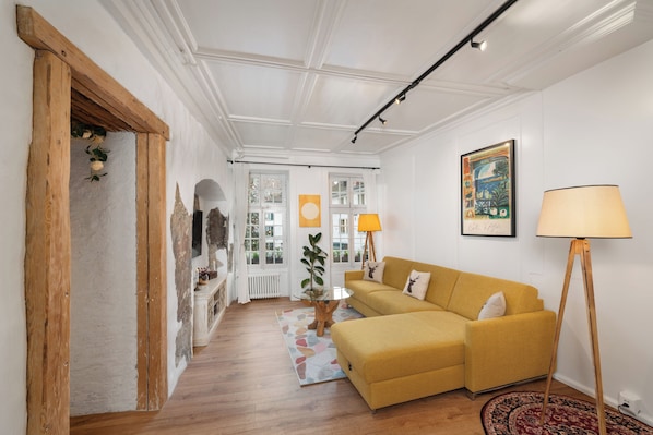 Ein Wohnzimmer mit gelbem Sofa, einer Stehlampe und einem gemusterten Teppich.