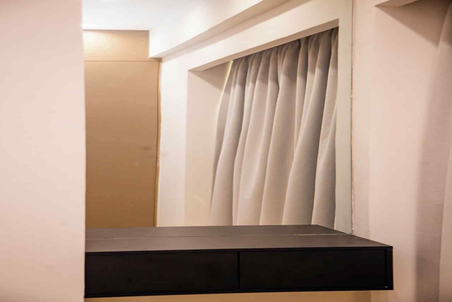 Habitació amb una cadira fixa, una finestra amb cortina i una porta.