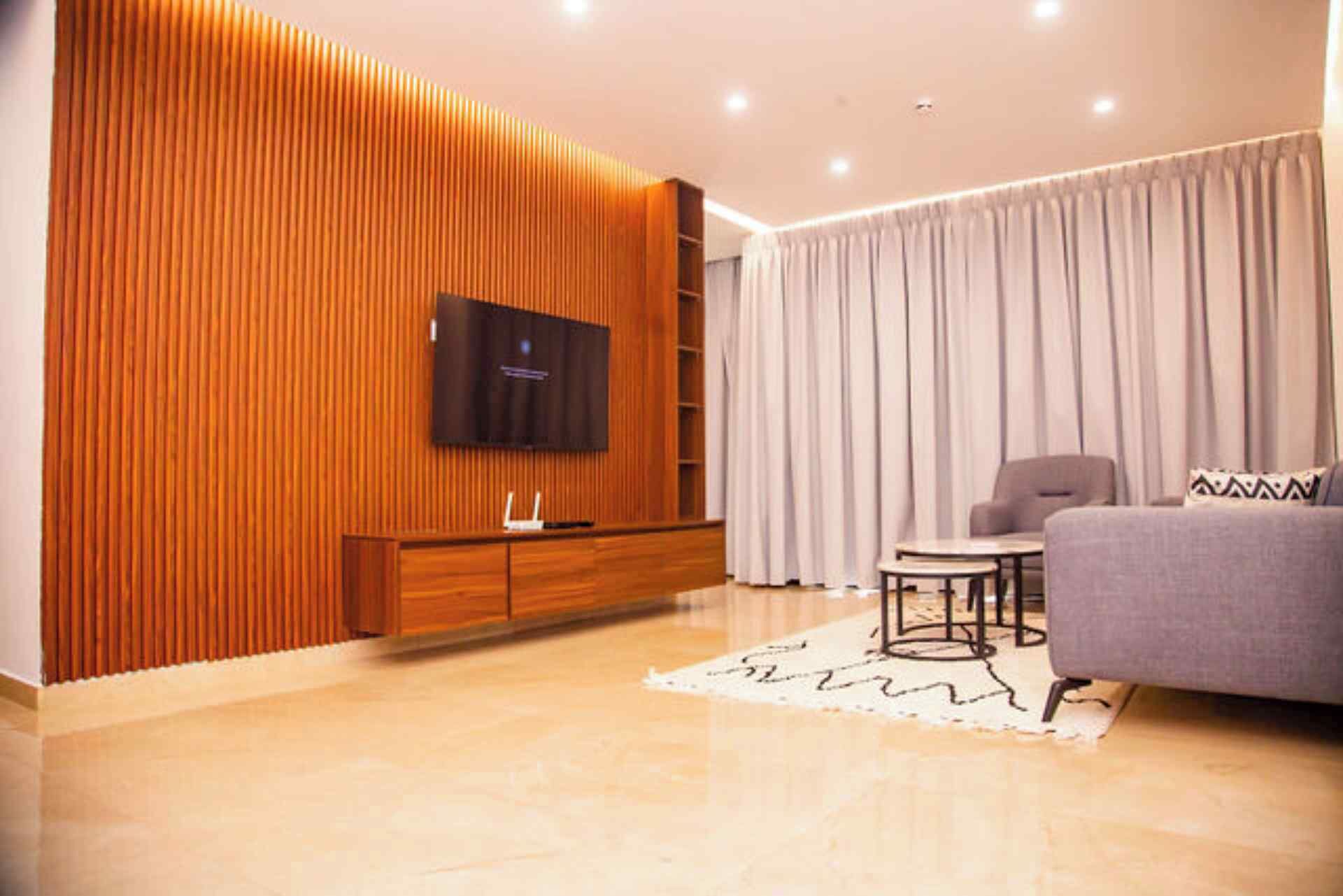 Un salon moderne avec un mur d’accent en bois, un téléviseur à écran plat, un canapé gris et un rideau blanc.