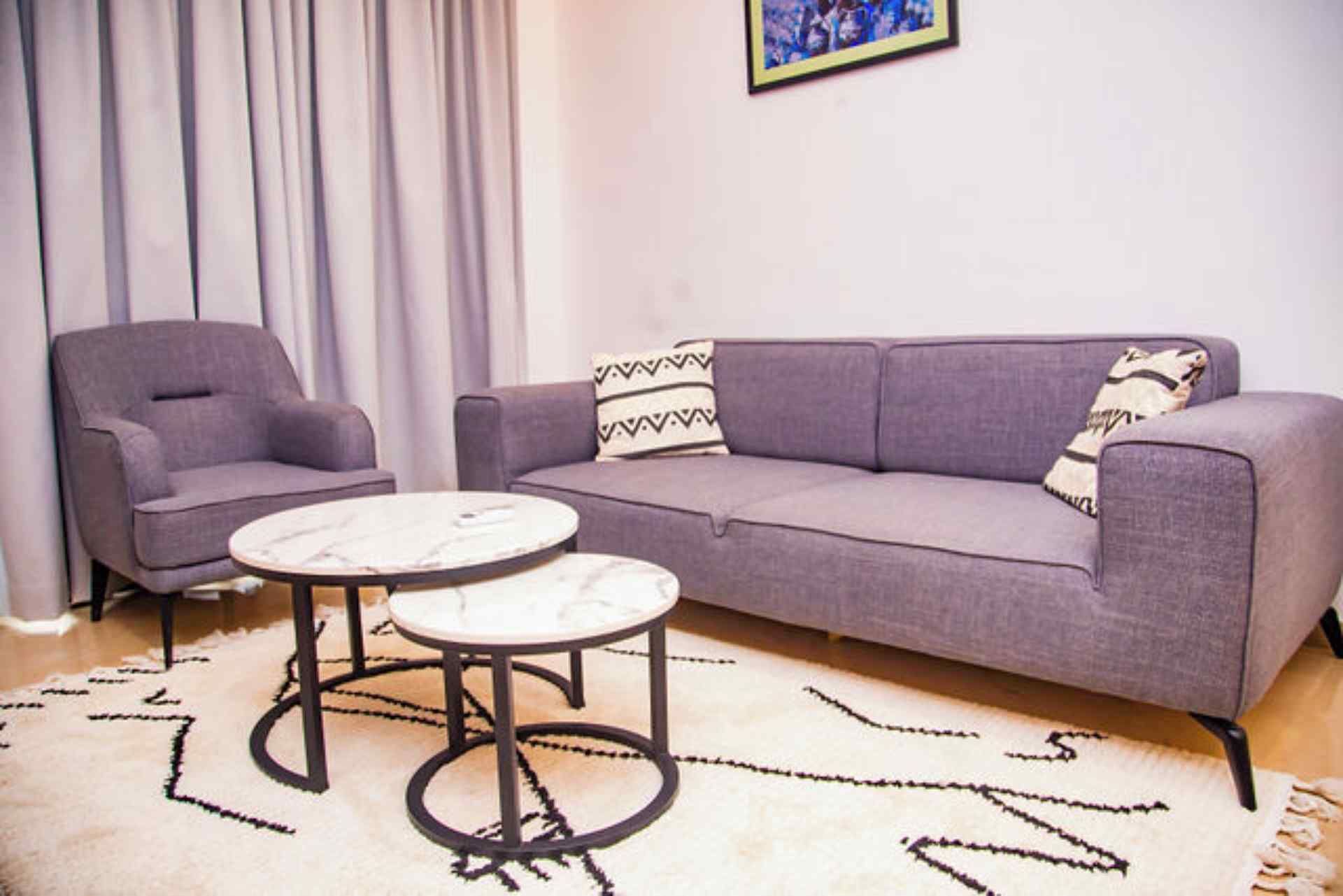 Un salon avec un canapé gris, deux fauteuils et une table basse ronde.
