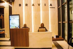 A reception desk with a wooden finish and a large screen. The word 'BRAVIA' is displayed above the desk, and 'Residency' is written to the right. - Bravia Residency - Spring Properties (Accra)