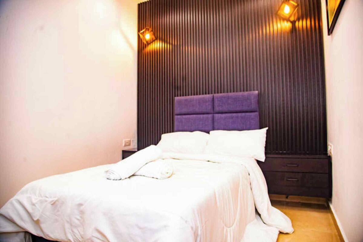 A bedroom with a bed, a headboard, and wall-mounted lights.