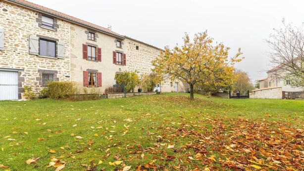 Ein Steingebäude mit roten Fensterläden, einer grünen Rasenfläche und verstreuten Herbstblättern.