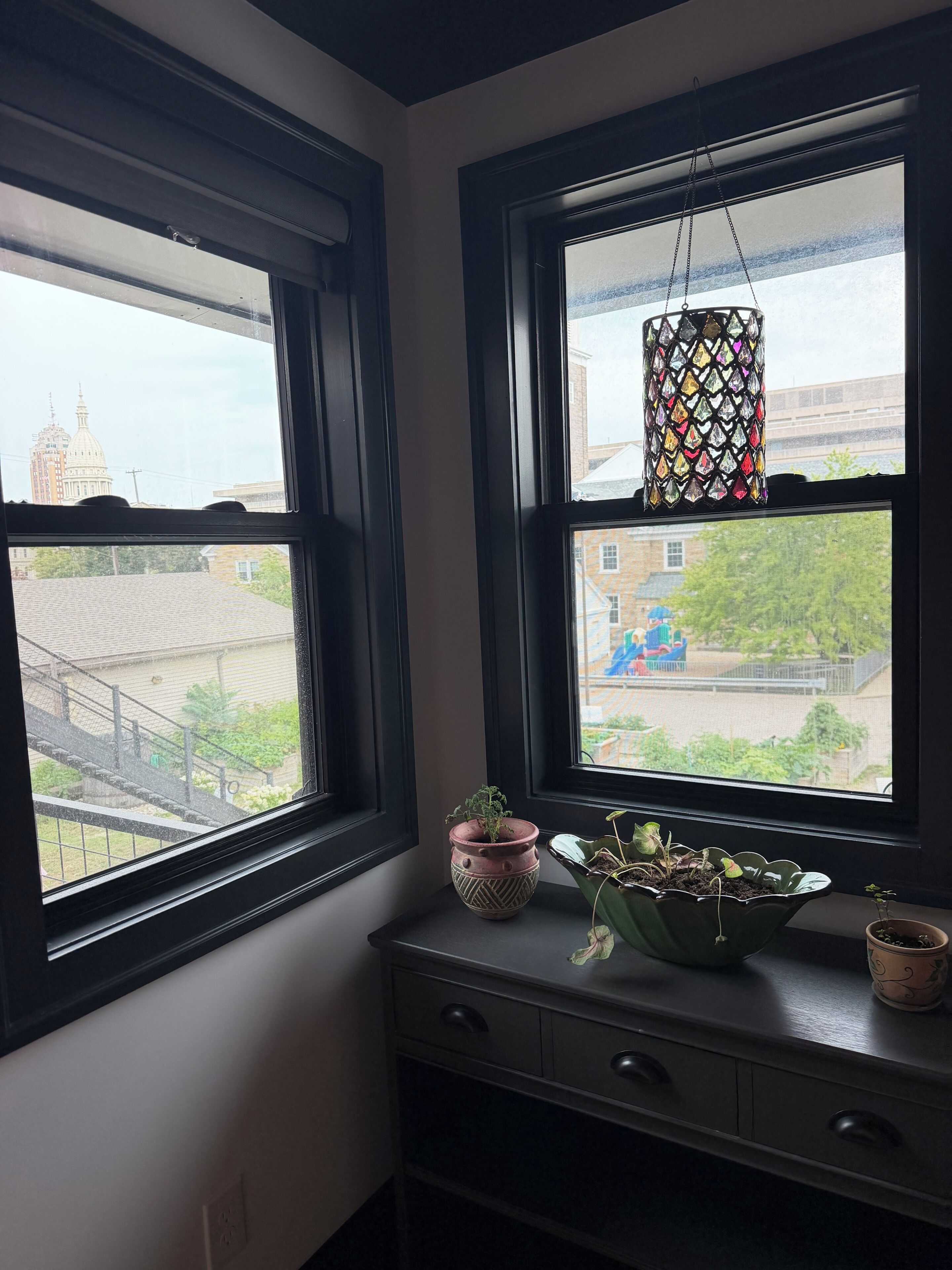 A room with two windows, a decorative hanging light, and a small plant on a dresser.