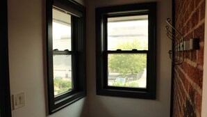 A room with two windows, a brick wall, and a metal rack on the right. - Urban Garden Loft - Historic Charm & Bold Design (Lansing)