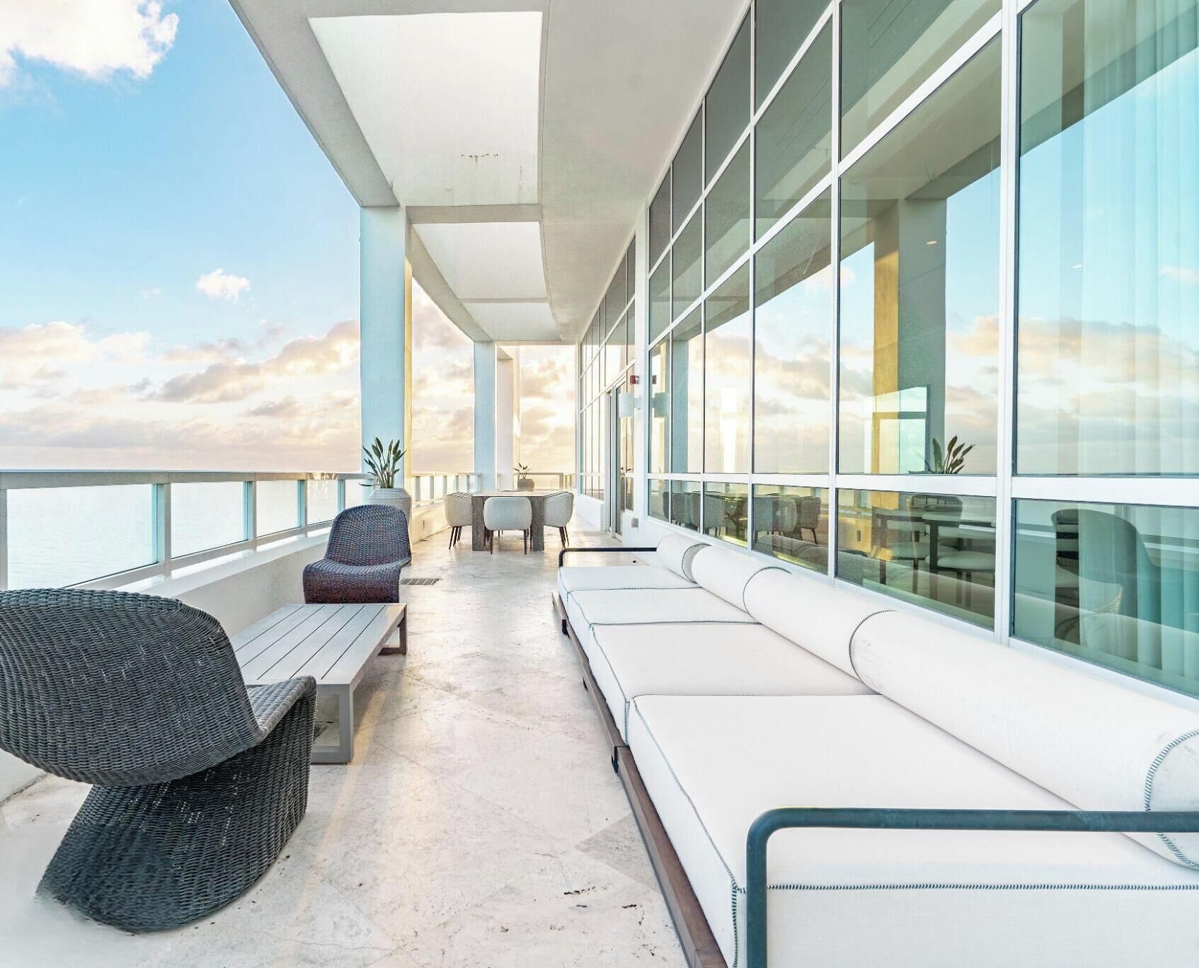 Un área de descanso al aire libre moderna con asientos, una mesa y grandes ventanales que ofrecen vistas al cielo.
