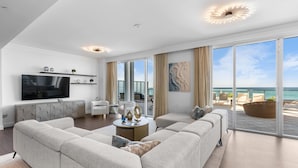 A modern living room with a large flat-screen TV, a sofa set, a coffee table, and a view of the ocean through large windows. - Sorrento 512 (Miami Beach)