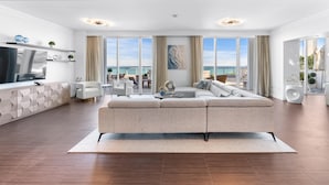 A modern living room with a large sectional sofa, a flat-screen TV, and a view of the ocean. - Sorrento 512 (Miami Beach)