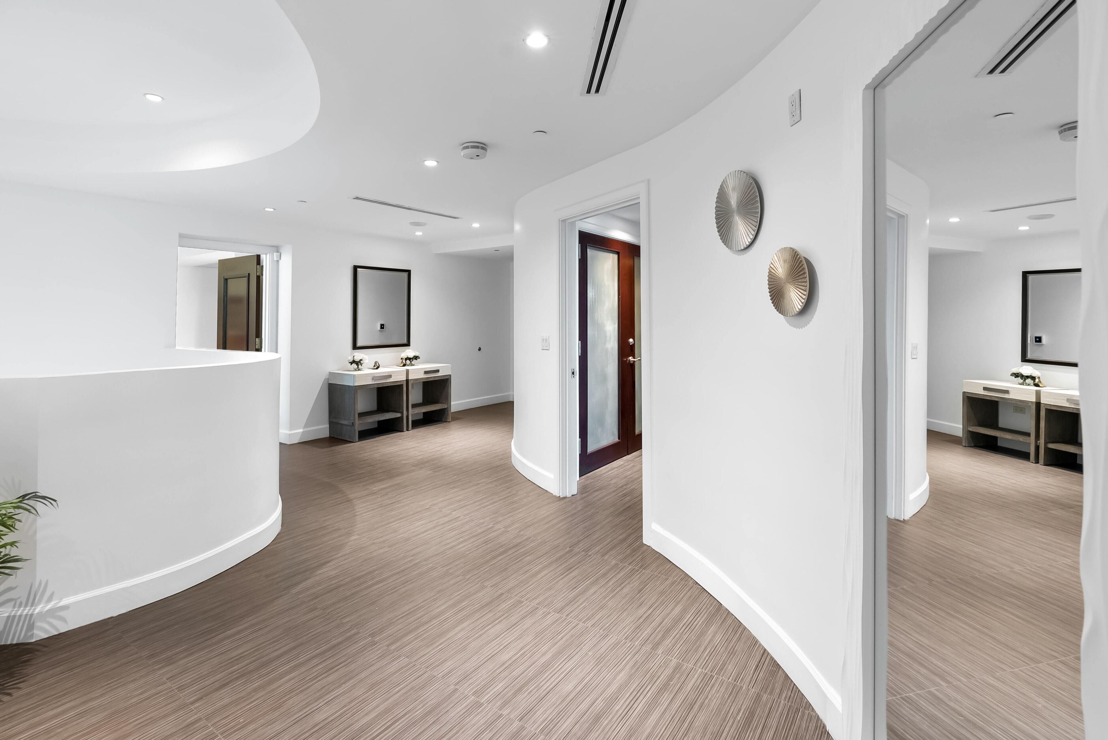 A modern hotel lobby with a curved reception desk, a mirror, and a wooden floor.