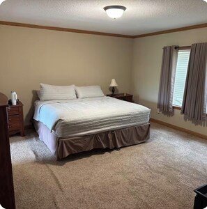 A bedroom with a bed, nightstand, lamp, and window with curtains. - Grand Lake Hideout (Jay)