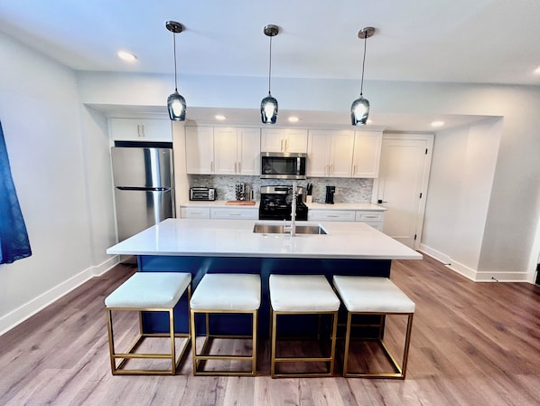 A modern kitchen with a central island, bar stools, stainless steel appliances, and pendant lighting.