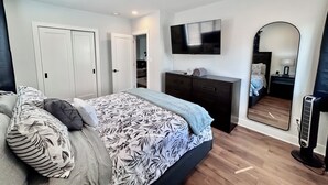 Un dormitorio con cama, cómoda, televisor, espejo y calefactor.