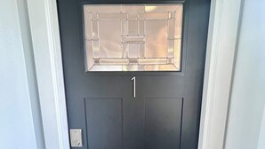 Una puerta oscura con el número '1' encima, un candado electrónico y un pequeño ventanal con diseño de cuadrícula.