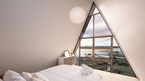 A bedroom with a large window, a bed, a dresser, and a hanging light fixture.