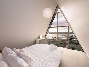 Un dormitorio con una ventana grande, una cama, un tocador y una lámpara colgante.