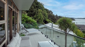 A modern balcony with a glass railing overlooking a lush green hillside and a body of water.