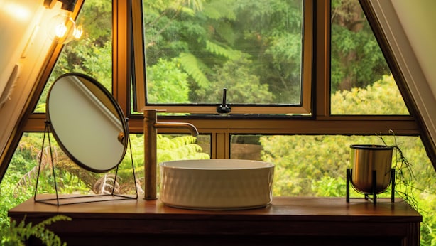 A room with a large window, a round mirror, a sink, and a potted plant.