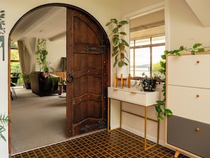 Una habitación con un gran puerta de madera, un escritorio blanco con cajones, un espejo y vistas a un balcón.