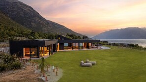 Une maison moderne dotée d’une grande façade vitrée, d’une pelouse bien entretenue et surplombant un paysage montagneux.