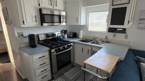 A compact kitchenette with a stove, microwave, and sink, a blue sofa, and a clock on the wall.