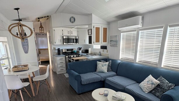 A modern living room with a blue sofa, a dining area with a white table, and a kitchen with white cabinets.
