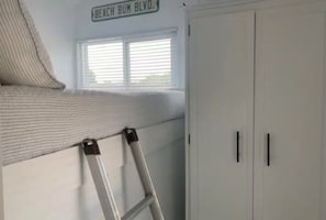 Una habitación con ventana, un armario blanco y una escalera apoyada en la pared.